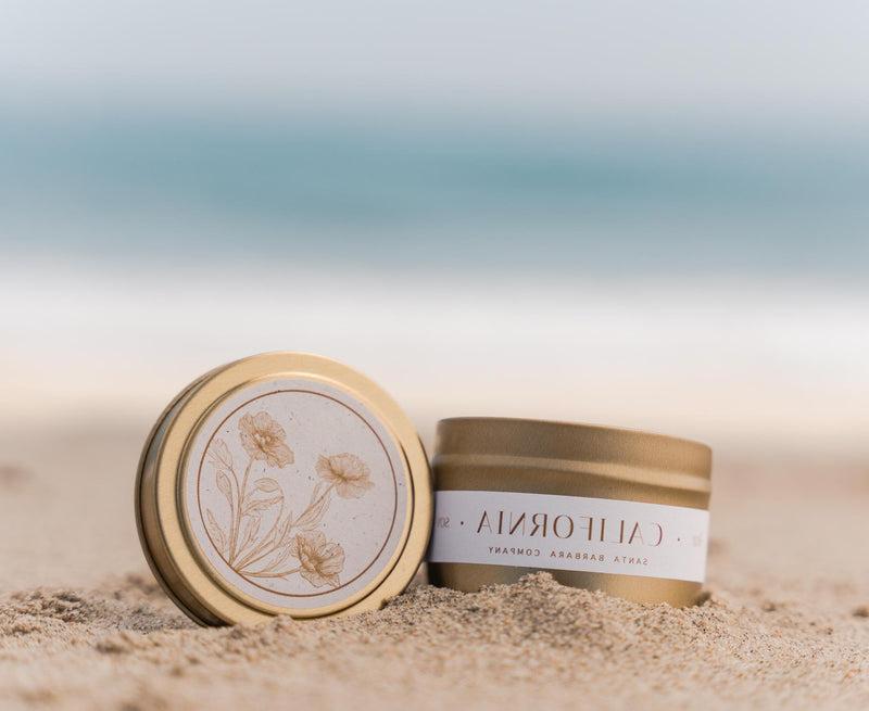 California travel candle with poppy design on lid shown on a beach
